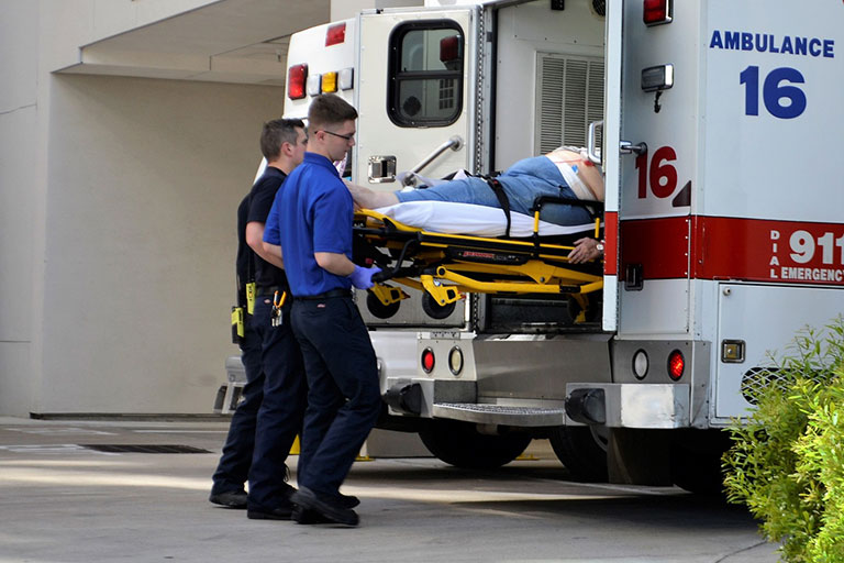 Ambulance attendants lifting an injured worker into a waiting ambulance.